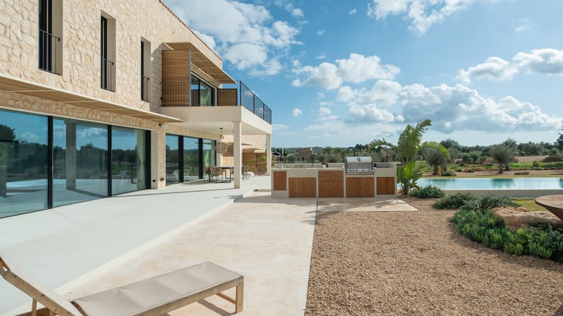 Modern terrass med utomhuskök i trä, naturstensfasad och stora fönsterpartier.