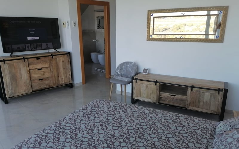 Chambre moderne avec consoles en bois rustique, grand téléviseur et vue sur la salle de bain privée.