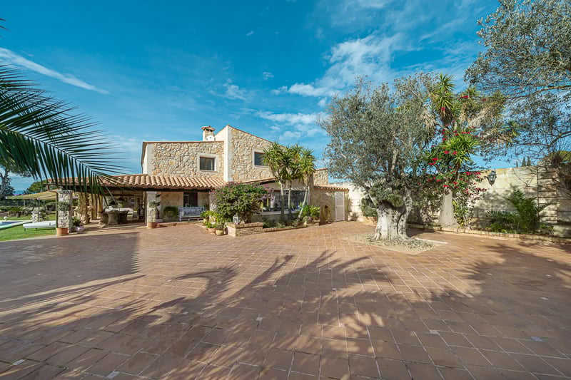 Grande terrasse en terre cuite avec olivier et bougainvilliers devant une villa en pierre sous un ciel bleu.
