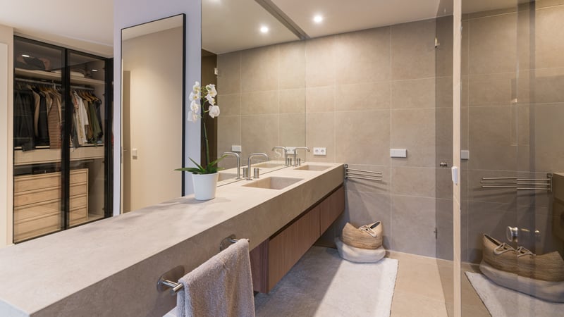 Modern bathroom featuring double stone vanity, large mirror, and glass-enclosed walk-in closet with internal lighting.