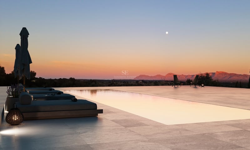 Piscine à débordement et terrasse en pierre au crépuscule surplombant des montagnes sous un ciel de coucher de soleil.