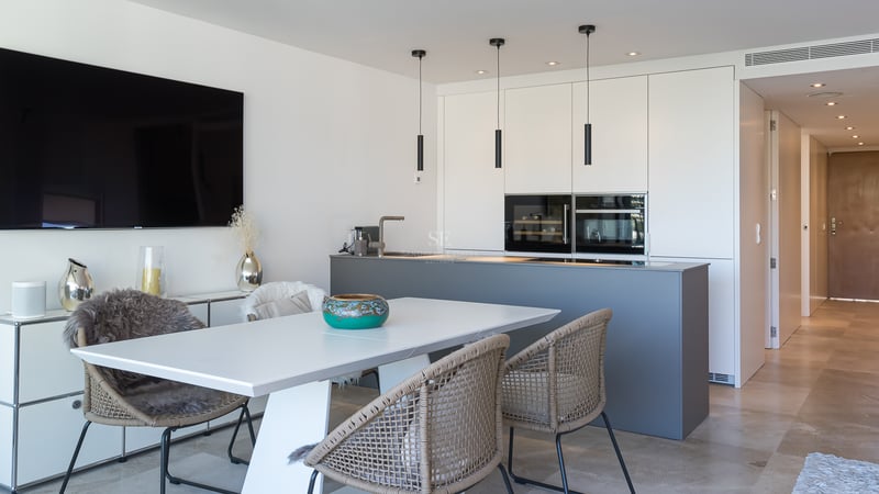 Moderne Küche mit grauer Kochinsel, grifflosen weißen Schränken und Essbereich mit Natursteinboden.