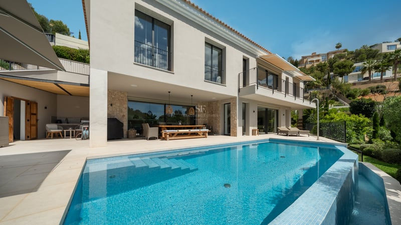 Vue piscine turquoise, jardin luxuriant, architecture moderne, façade blanche, larges fenêtres, reflets de lumière, ciel bleu.