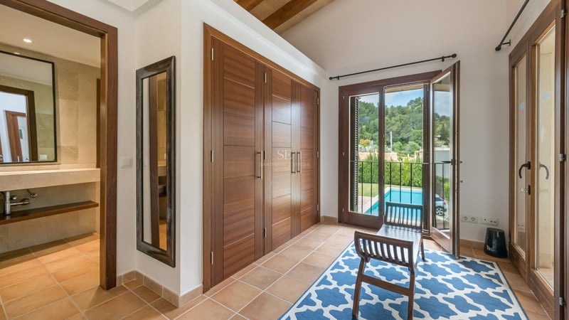 Chambre lumineuse avec grands placards en bois, sol en terre cuite et vue sur une piscine.