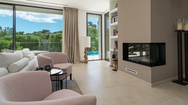 Salon lumineux avec grandes baies vitrées offrant une vue sur la mer. Intérieur moderne avec canapé beige, table basse et détails décoratifs élégants.