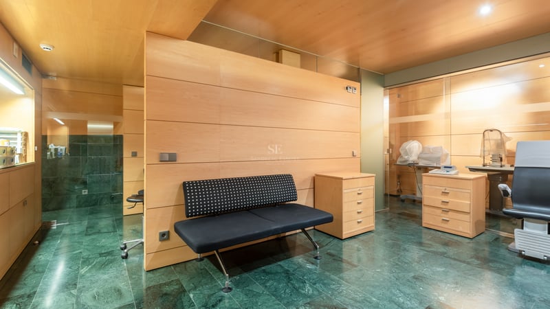 Intérieur avec sol en marbre vert, boiseries claires, banc noir et équipement de consultation médicale.
