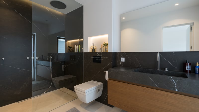 Salle de bain moderne avec murs en marbre noir, toilettes suspendues, vanité en bois et douche à l'italienne vitrée.
