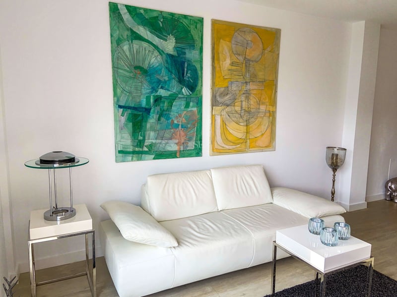 Weißes Ledersofa mit abstrakten Gemälden in Grün- und Gelbtönen sowie minimalistischen Chrommöbeln.