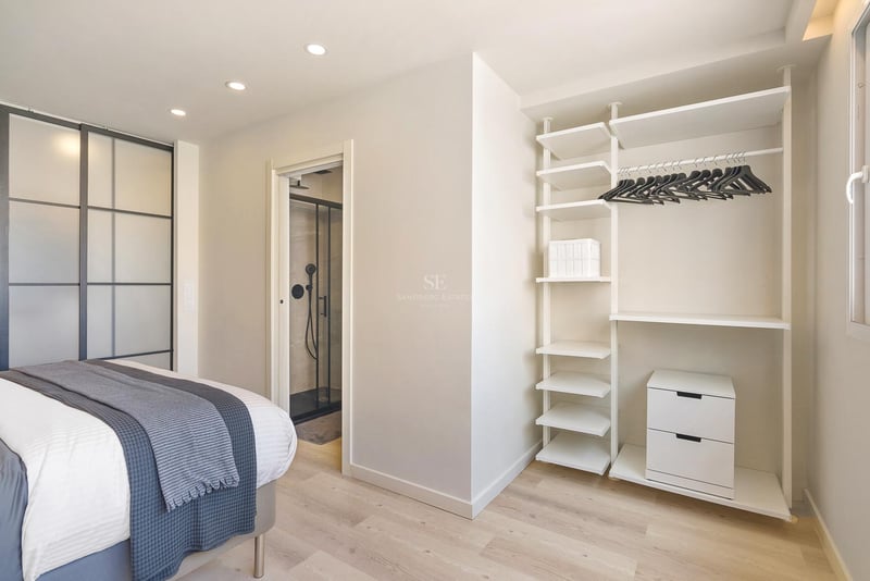 Helles modernes Schlafzimmer mit offenem weißem Schranksystem, hellem Echtholzparkett und Blick ins angrenzende Badezimmer.