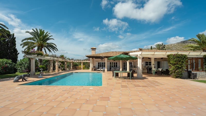 Grande piscine rectangulaire entourée d'une terrasse en terre cuite et d'une villa blanche sous un ciel bleu.