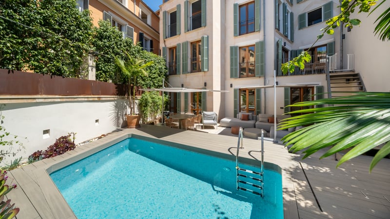 Une piscine turquoise dans une cour privée entourée d'un bâtiment à plusieurs étages avec des volets verts.