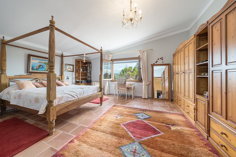 Chambre avec lit à baldaquin en bois, sol en terre cuite et grandes armoires sous un lustre en cristal.