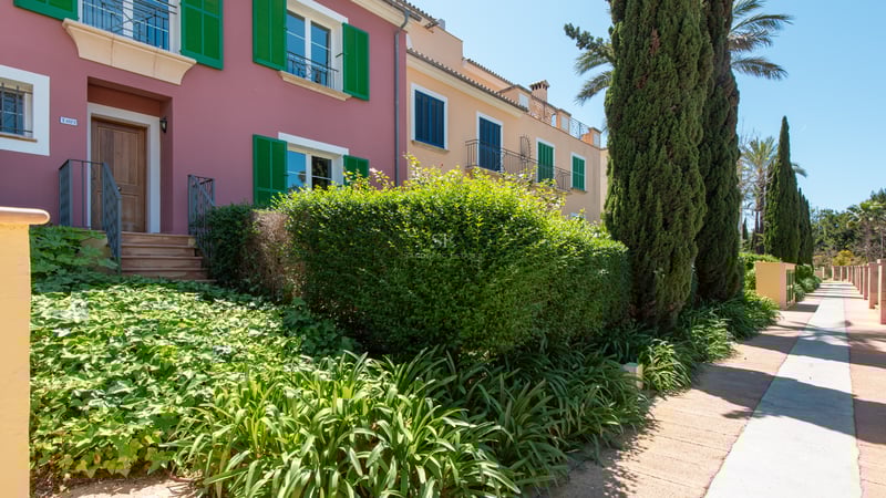 Colorful Mediterranean townhouses with green and blue shutters, surrounded by cypress trees and manicured gardens.