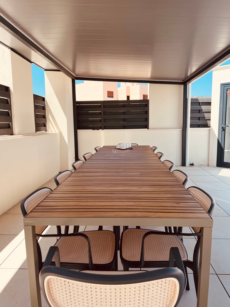 Une longue table à manger d'extérieur en bois avec dix chaises sous une pergola moderne sur une terrasse ensoleillée.