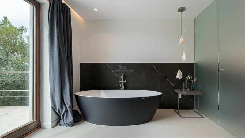 Salle de bain moderne avec baignoire îlot noire ovale devant un mur en marbre sombre et lumière naturelle.