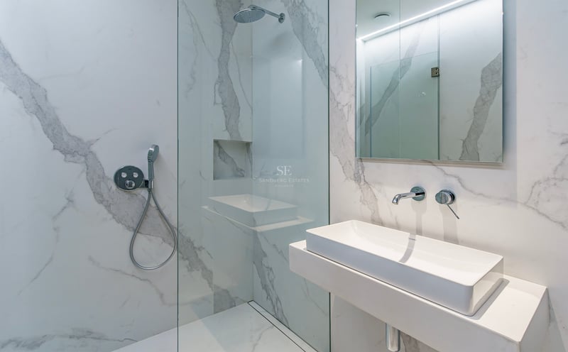 Salle de bain moderne avec carrelage effet marbre blanc, douche à l'italienne vitrée et lavabo minimaliste.