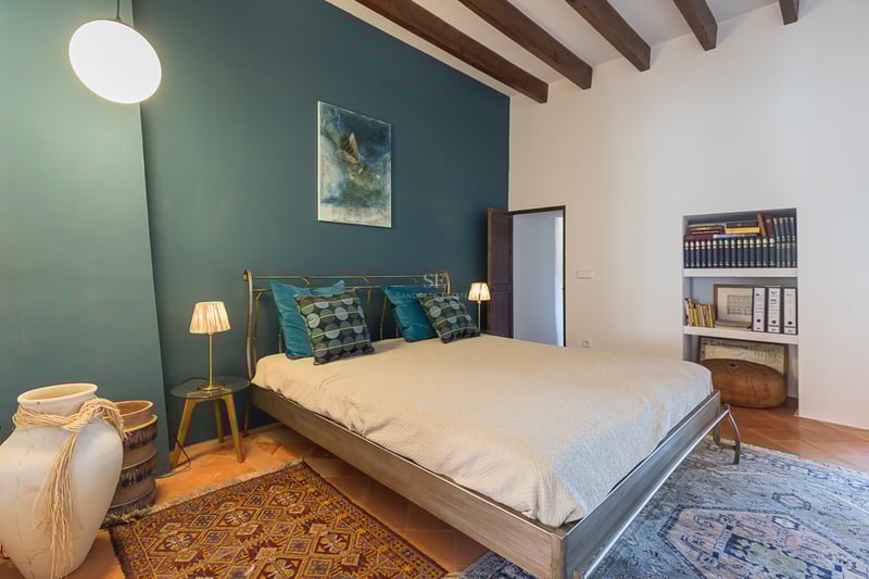 Chambre avec mur d'accent bleu canard, poutres en bois, sol en terre cuite et lit en métal.