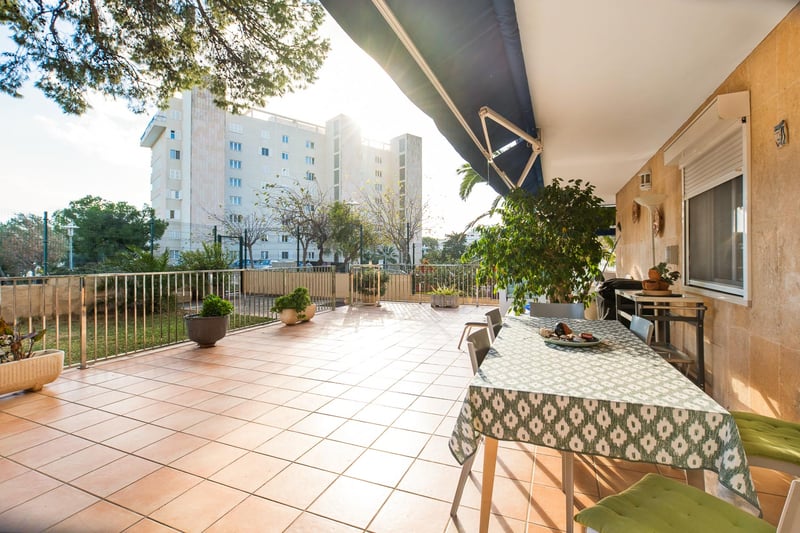 Weite Außenterrasse mit Terrakotta-Fliesen, Esstisch unter einer Markise und Natursteinwänden im Sonnenlicht.