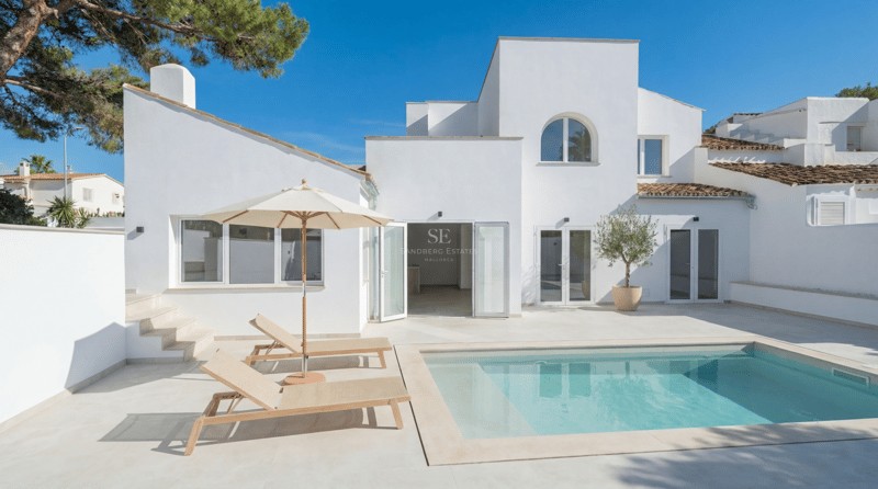 Villa contemporaine blanche avec piscine rectangulaire, terrasse en pierre claire et chaises longues sous un ciel bleu.