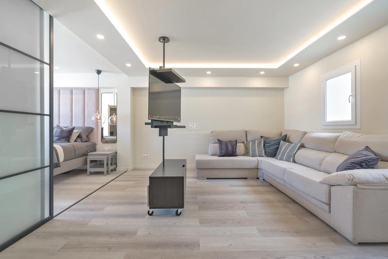 Zeitgenössisches Wohnzimmer mit großem beigem Ecksofa, drehbarem TV-Halter und angrenzendem Schlafbereich mit Glastrennwand.