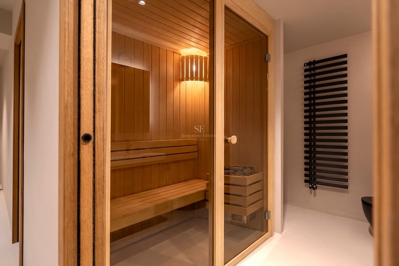 Sauna en bois clair avec porte vitrée, bancs à plusieurs niveaux et éclairage intérieur chaleureux.