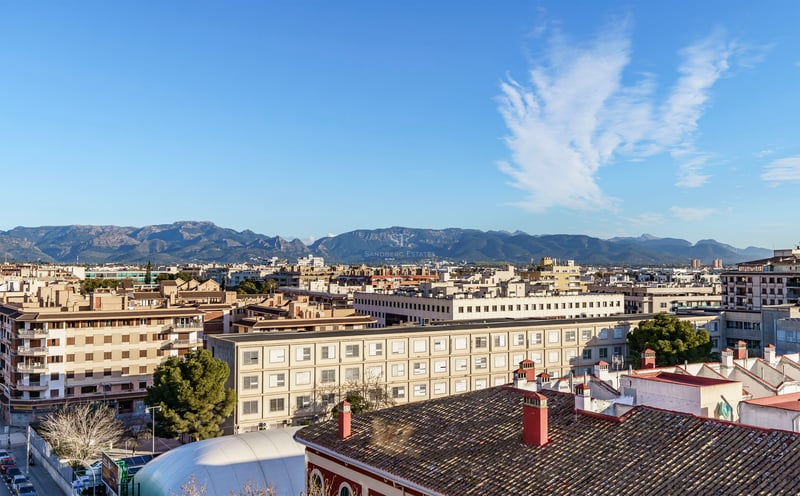 Vue surélevée sur les toits de la ville vers une chaîne de montagnes lointaine sous un ciel bleu.