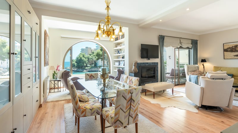 Ljus matsal med glasbord och ett stort bågfönster med utsikt över havet och kustlandskapet.