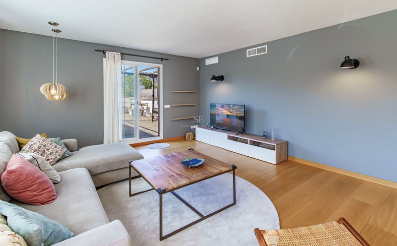 Ljust vardagsrum, grå väggar, ekparkett, hörnsoffa och glasdörr mot en träterrass.