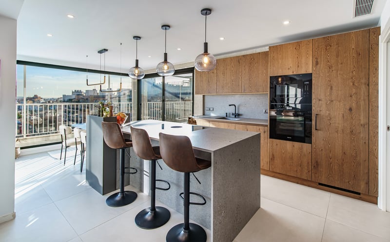 Cuisine moderne avec îlot en pierre, tabourets en cuir et grandes fenêtres offrant une vue panoramique sur la ville.