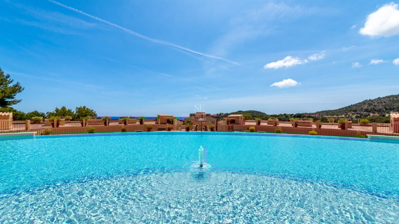 Grande piscine incurvée avec fontaine centrale et vue panoramique sur les bâtiments méditerranéens et la mer.