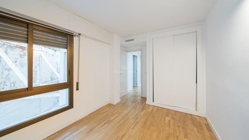 Tomt rum med ljust trägolv, en vit inbyggd garderob och ett stort fönster med bronsfärgad ram.