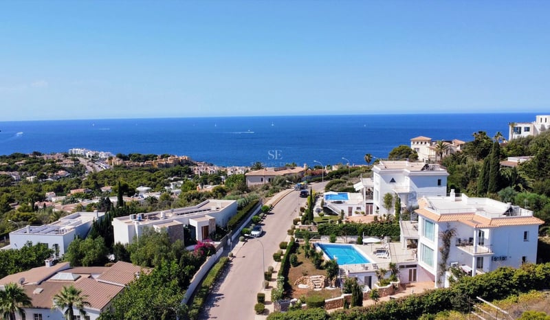 Vue aérienne de villas de luxe blanches avec piscines donnant sur la mer Méditerranée sous un ciel bleu clair.