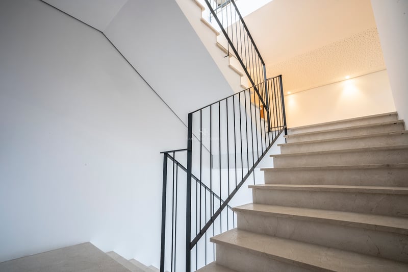 Cremefarbene Marmortreppe mit schwarzem Eisengeländer vor weißen Wänden bei natürlichem Licht.