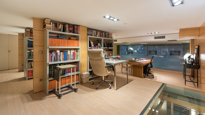 Bureau moderne avec parquet clair, étagères intégrées, bureau en verre et fauteuil ergonomique en cuir.
