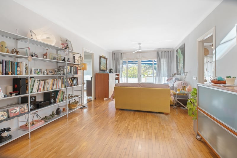 Großzügiges Wohnzimmer mit honigfarbenem Eichenparkett, großem Metallregal und Glasschiebetüren zum Balkon.