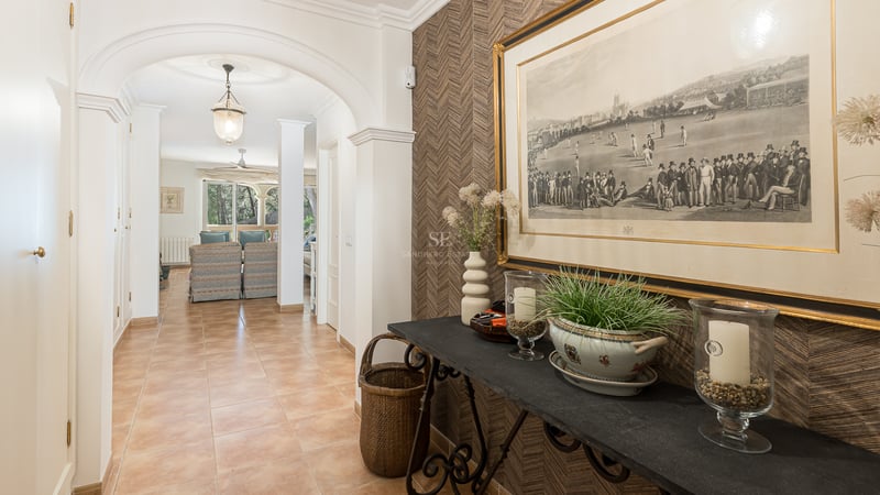 Bright hallway with terracotta tiles, white archways, and a decorated console table leading towards the living area.