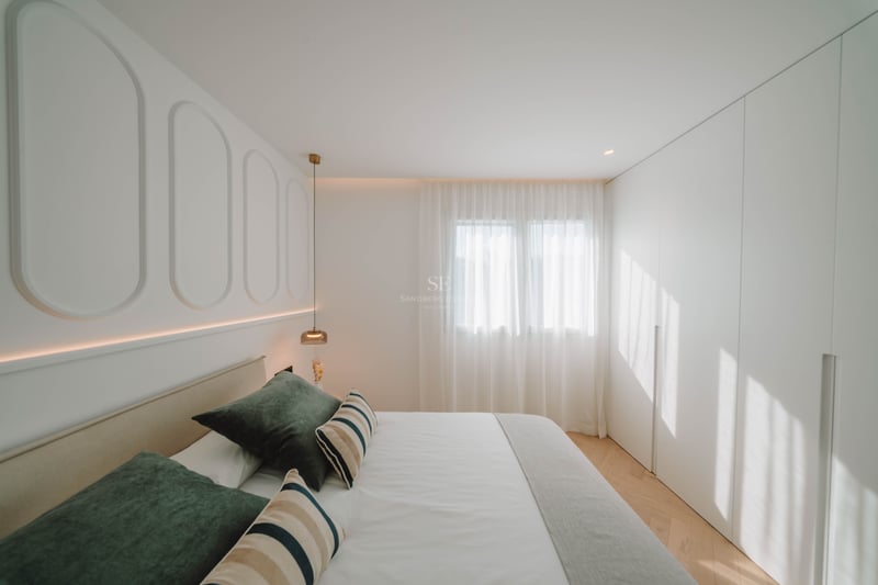 Chambre lumineuse avec panneaux blancs, lit aux coussins verts, parquet en chevrons et placards intégrés.