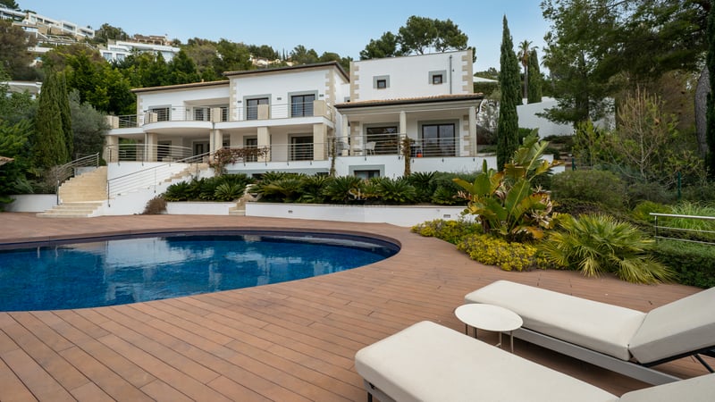 Villa de luxe blanche avec piscine incurvée, terrasse en bois et bains de soleil dans un cadre paysager.