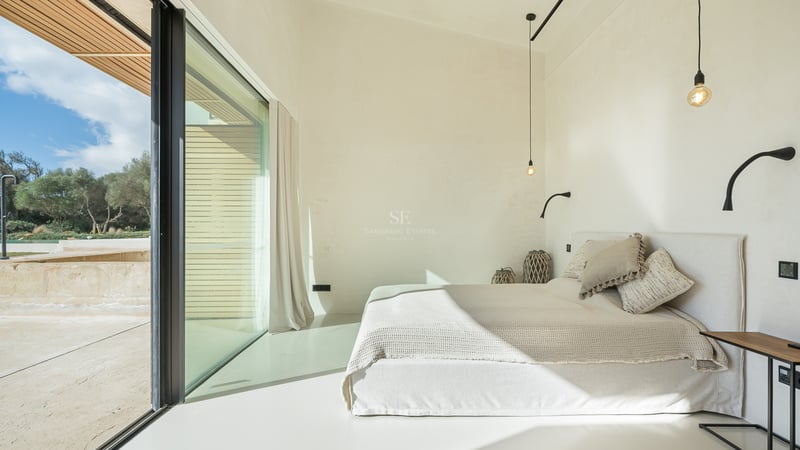 Ljust minimalistiskt sovrum med vit säng, stora glaspartier och privat balkong.