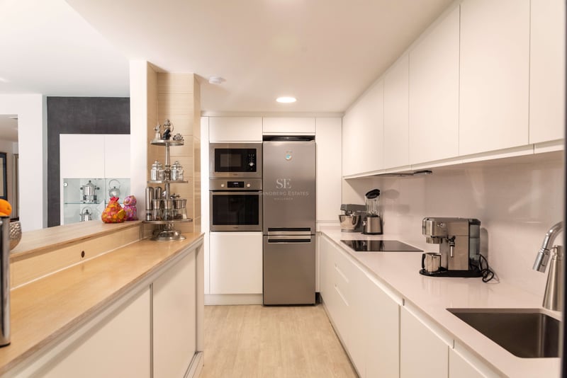 Saubere, moderne Küche mit weißen Schränken, Edelstahlgeräten und einer Frühstücksbar aus hellem Holz.