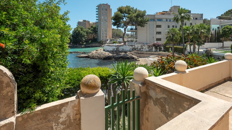 Utsikt över en turkos vik och stenig kustlinje från en medelhavsterrass med stenmurar.