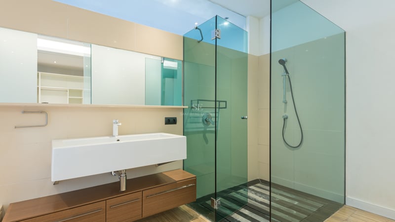 Modernt badrum med ett rektangulärt tvättställ, svävande träkommod och duschkabin i tonat glas.