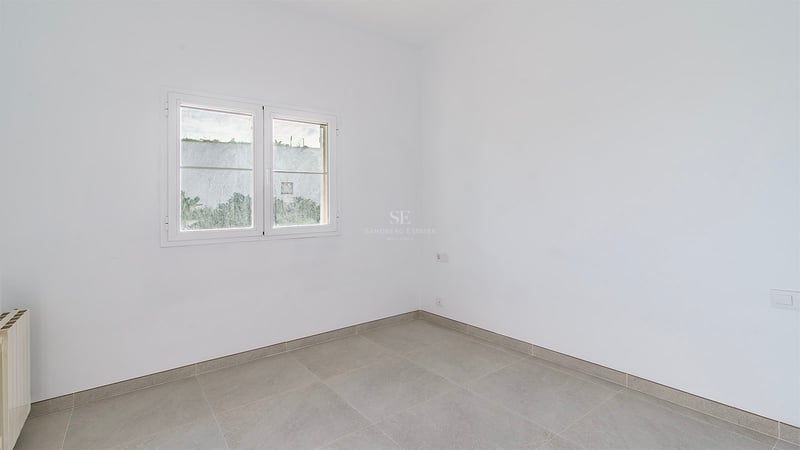 Tomt vitt rum med grå stengolv, tvåglasfönster och ett väggmonterat element.