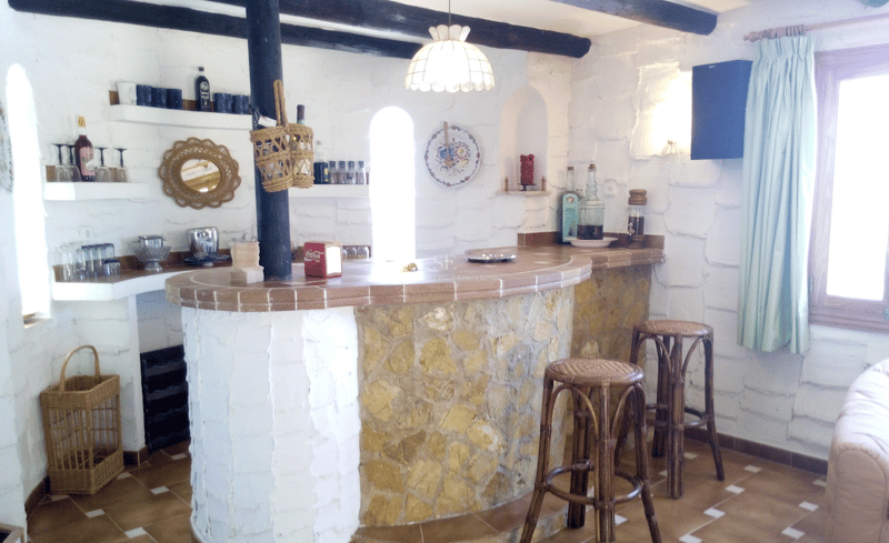 Un bar interior con base de piedra curva, encimera de baldosas de terracota y vigas de madera oscura en el techo.