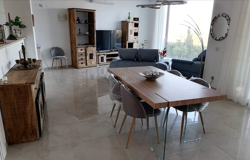 Grand salon et salle à manger avec carrelage poli, meubles en bois et table de repas avec pieds en verre.