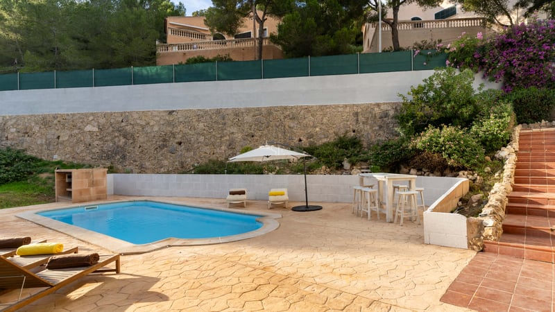 Piscine privée avec chaises longues, parasol blanc et mur en pierre rustique en arrière-plan.