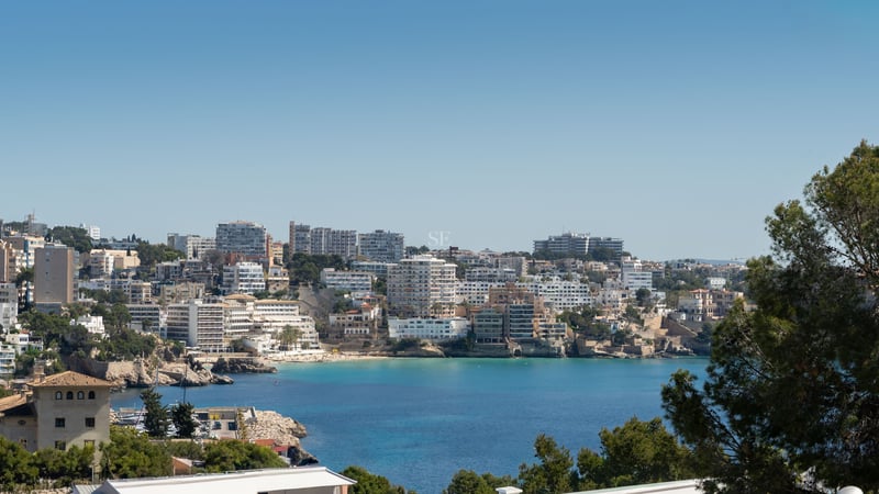 Panoramablick auf eine türkisfarbene Meeresbucht mit weißer Küstenbebauung unter strahlend blauem Himmel.