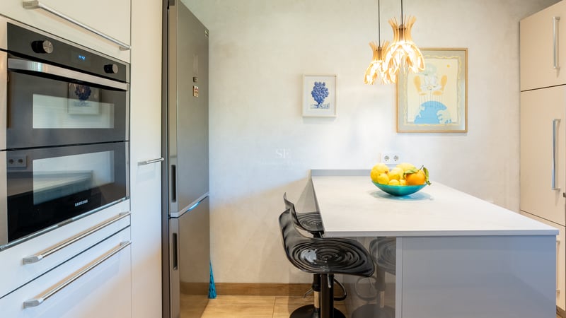 Samtida kök med Samsung dubbelugn, kylskåp i rostfritt stål och frukostö med svarta barstolar.