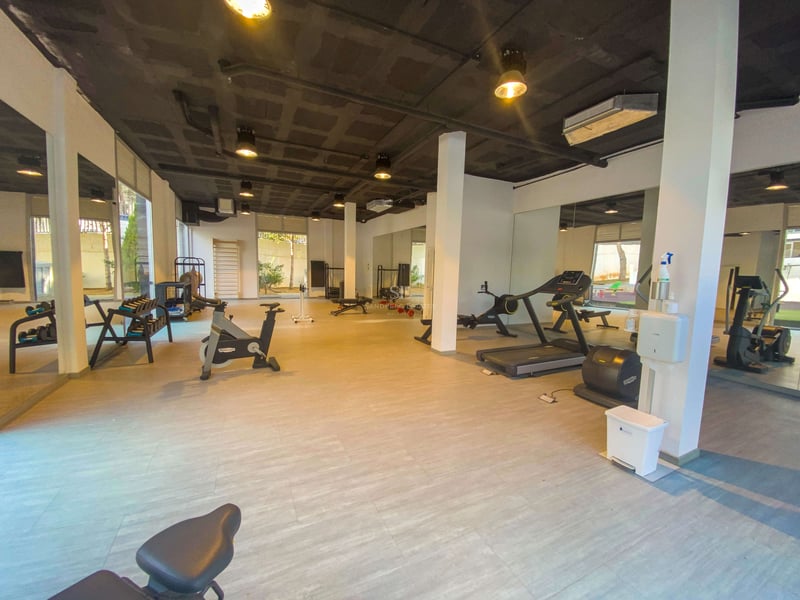 Geräumiges Fitnessstudio mit Technogym-Geräten, bodentiefen Spiegeln und industrieller Betondecke.