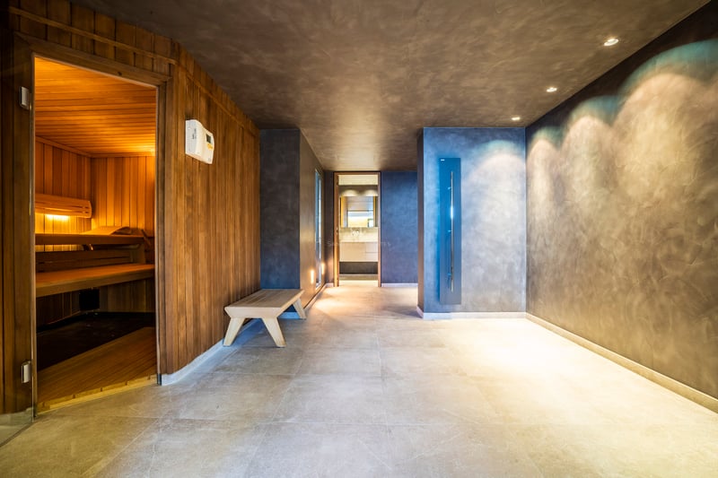 Moderner Indoor-Spa mit Holzsauna, grauen Mikrozementwänden und großformatigen Bodenfliesen.